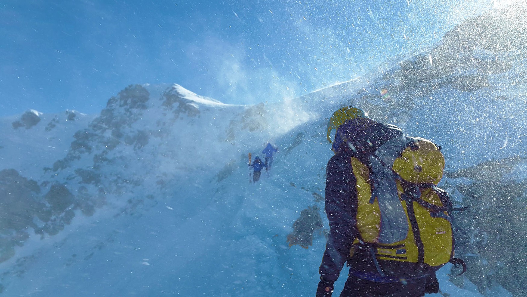 Mountaineer climbing a snowy mountain in harsh weather conditions.